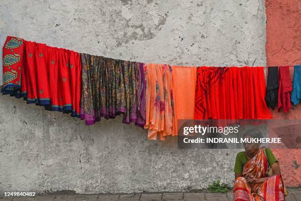 Woman waits for her clothes to dry on a footpath in Mumbai on March 29, 2023.