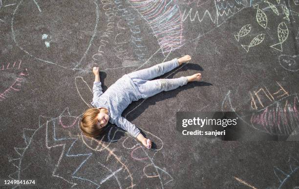 young boy lying down on the asphlat doodled with chalk - child lying down stock pictures, royalty-free photos & images