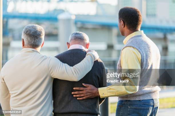 drei multiethnische männer hängen an einer stadtufer - dreiviertel rückansicht stock-fotos und bilder