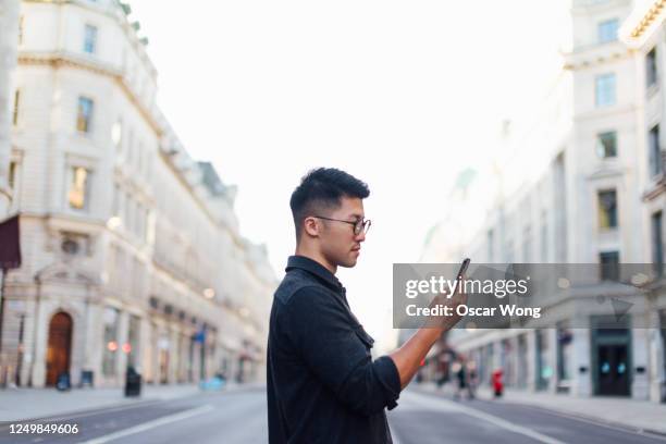 confident man exploring the city with smartphone - street side stock-fotos und bilder