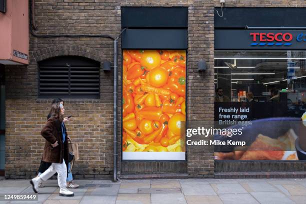 Supermarket poster advertising a selection of orange fresh food available including oranges, carrots and peppers outside Tesco Express on 27th March...