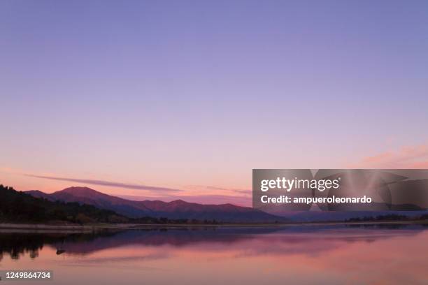 beau paysage de patagonie de la chaîne de montagnes des andes avec de hautes montagnes avec des sommets illuminés, des pierres dans le lac de montagne, la réflexion, le ciel violet et le brouillard au coucher du soleil. - violette photos et images de collection