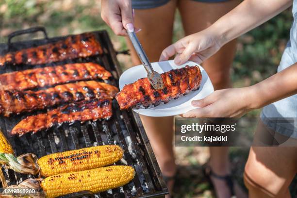 jonge vrouw die varkensvleesribben op de barbecuegrill in de binnenplaats voorbereidt - backyard grilling stockfoto's en -beelden