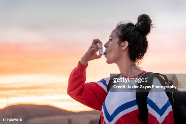 millennial woman using her asthma inhaler at the lake shore at sunset - asthmainhalator stock-fotos und bilder