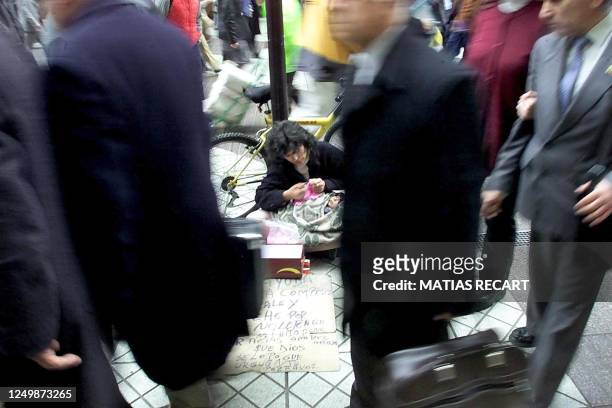 Woman begs with her son on a central Santiago street, Chile, while a group of businessmen passes next to her, 11 July 2001. Una mujer con su hijo...
