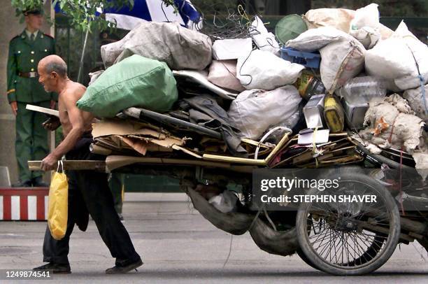 An elderly Chinese migrant pulls his old wooden wagon full of recyclable trash through Beijing's affluent embassy district 19 May 2000. Tens of...