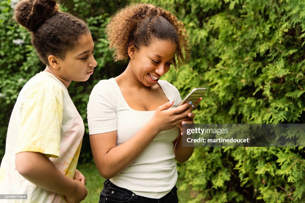 Gemengde tienerzusters die mobiele telefoon in binnenplaats bekijken.