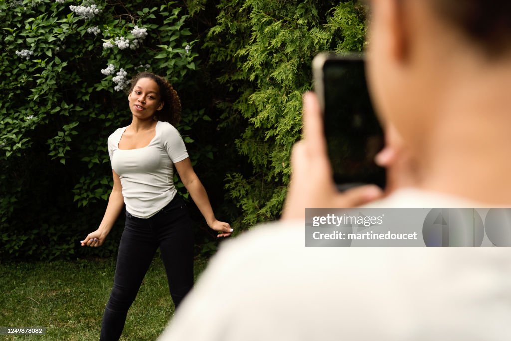 Mixed-race teenage sisters filming with mobile phone in backyard.