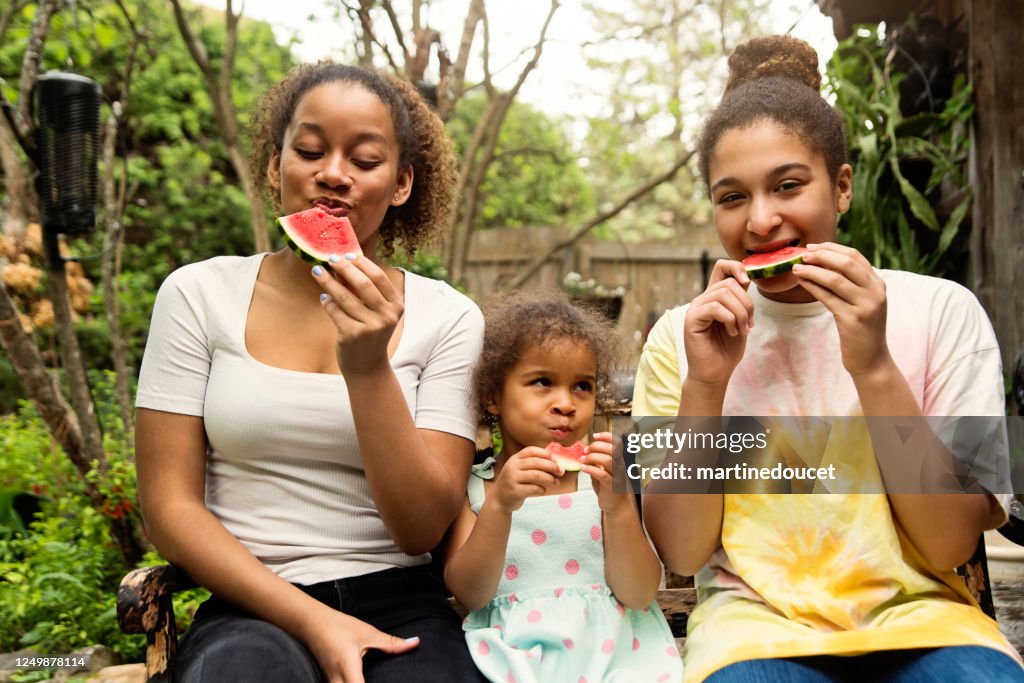 Hermanas de raza mixta comiendo sandía en el patio trasero.