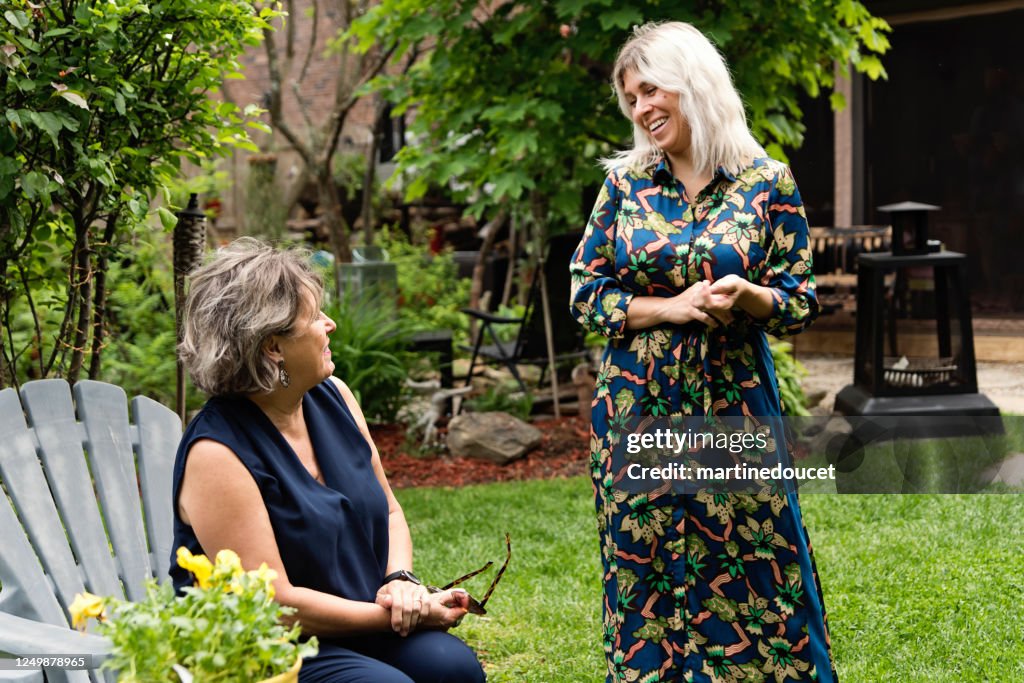 Adult daughter and senior mother chatting backyard.