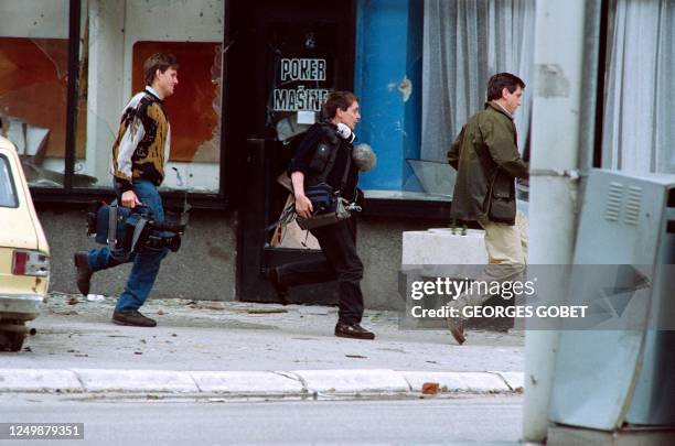 Journalist and a TV crew run for cover in a street to avoid snipers who are posted in evacuated houses in the Bosnian Capital, on May 31, 1992.
