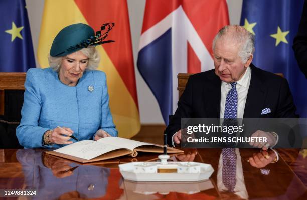 Britain's King Charles III looks on as Britain's Camilla, Queen Consort signs the guest book at the presidential Bellevue Palace in Berlin, on March...