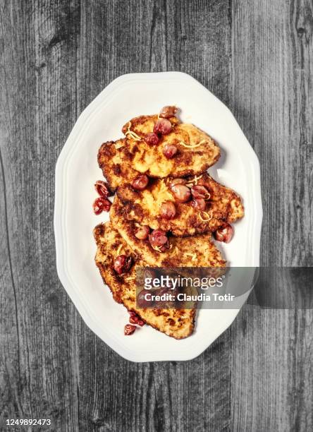 schnitzel with roasted red grapes on a plate on wooden, black background - wiener schnitzel stock pictures, royalty-free photos & images