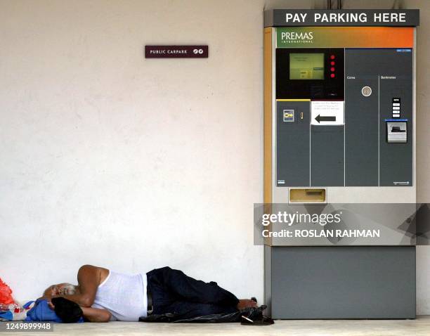 Man in sleeps away from the noise of the street next to a carpark payment machine in Singapore, 26 August 2002. More than half of the Singaporeans...