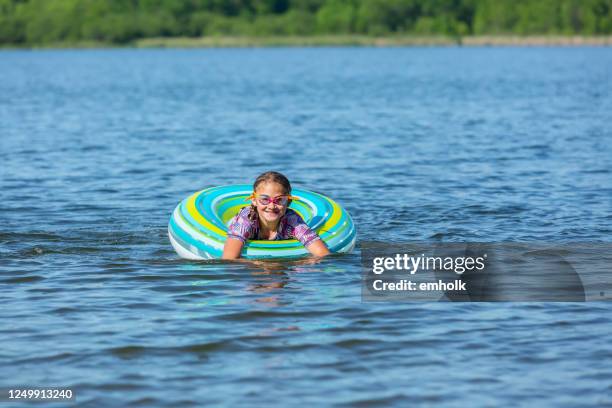 meisje dat op meer in gestreepte binnenband vlotter toy drijft - swimming tube stockfoto's en -beelden