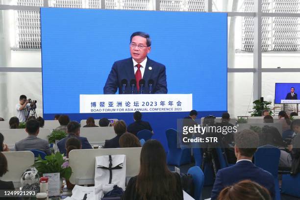 Journalists watch a screen showing China's Premier Li Qiang delivering a speech during the opening of the Boao Forum for Asia in Boao, south China's...
