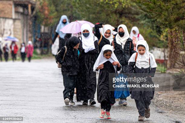 Afghan school girls walk amid rainfall along a road in Paghman district on the outskirts of Kabul on March 30, 2023.