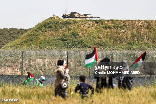 The turret of an Israeli Merkava battle tank is seen across the border with the Gaza Strip as Palestinian protesters gather along the fence during...