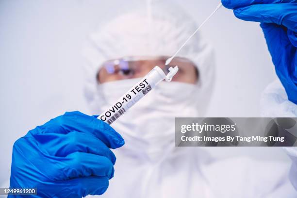 doctor in protective gloves & workwear holding open test tube and taking out sampling swab for novel covid-19 test - à prova de covid 19 - fotografias e filmes do acervo