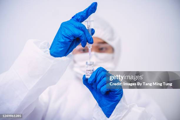 doctor in protective gloves & workwear filling injection syringe with covid-19 vaccine - inmunología fotografías e imágenes de stock