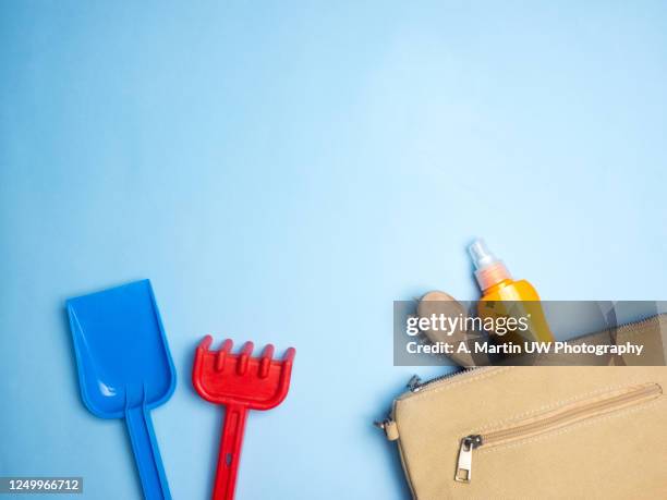 beach toys (shovel and plastic rake) and bag with brush and suntan lotion on a light blue background - beach shovel stockfoto's en -beelden