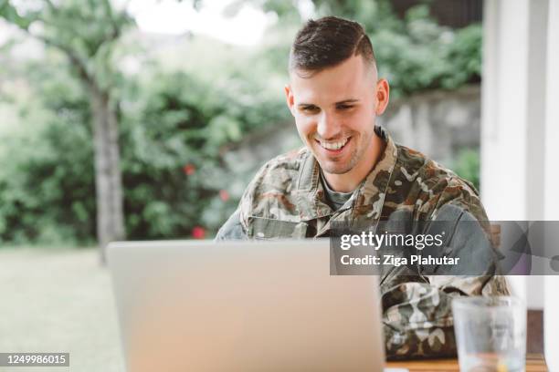smiling man in army uniform calling home from a mission - soldado-exército imagens e fotografias de stock