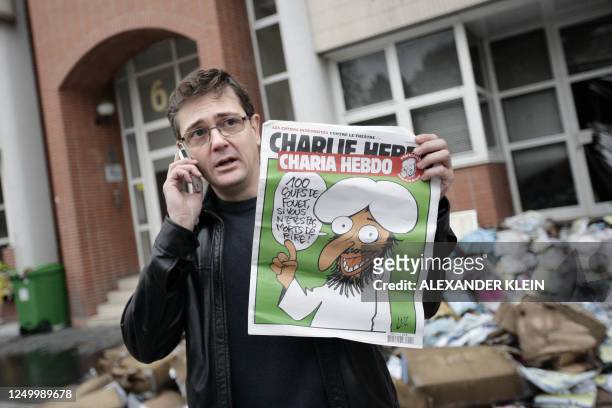 The Charlie Hebdo's publisher, known only as Charb, uses his cell phone as he shows a special edition of French satirical magazine Charlie Hebdo on...