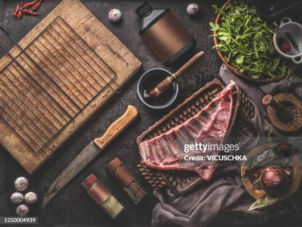 raw lamb ribs on dark rustic kitchen table background with bbg ingredients, spices and sauce, wooden cutting board with grill grate top view. - lamm fleisch stock-fotos und bilder