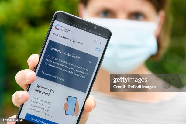 In this photo illustration, The main page of the Corona Warn app is seen on an Andriod smartphone. The smartphone is held by a woman with a...