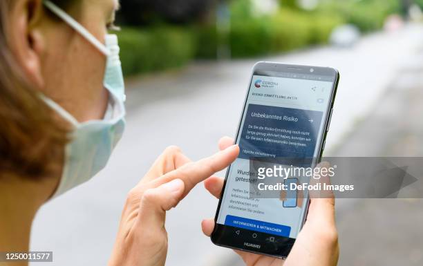 In this photo illustration, a woman with a protective mask is seen. She holds a smartphone in her hand with the main page of the Corona Warn app on...