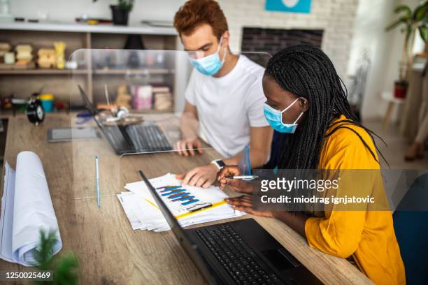 coworkers with protective face masks looking at graph and talking about business strategy at office - covid reopening stock pictures, royalty-free photos & images