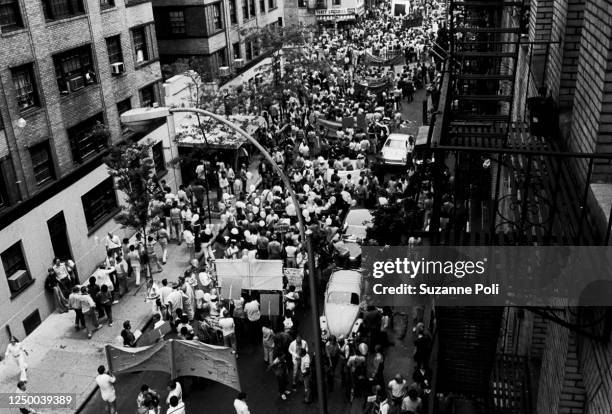 View, looking east, along on Christopher Street of pedestrians, onlookers, and marchers, some with signs and banners, during the annual New York City...