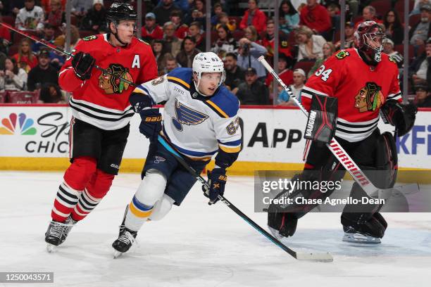 Jake Neighbours of the St. Louis Blues looks up the ice next to Connor Murphy and goalie Petr Mrazek of the Chicago Blackhawks in the second period...