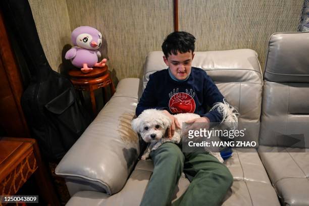 This picture taken on March 29, 2023 shows Victor Liu, a 14-year-old Beijinger with visual impairment and autism, holding his dog as he rests at home...