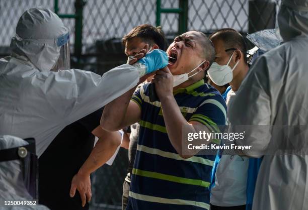 Chinese epidemic control worker wears a protective suit and mask while performing a nucleic acid test for COVID-19 on a man who has had contact with...