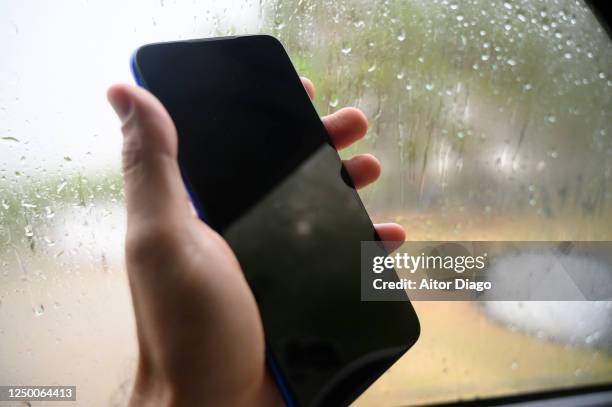 mas hand holding with a mobile phone inside a car while raining outside, germany. - car splashing water on people stock pictures, royalty-free photos & images