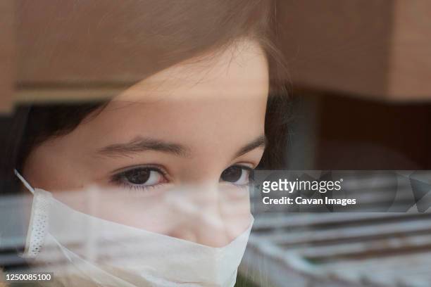 girl with face mask looking out the window quarantined by coronavirus - sistema inmunocomprometido fotografías e imágenes de stock