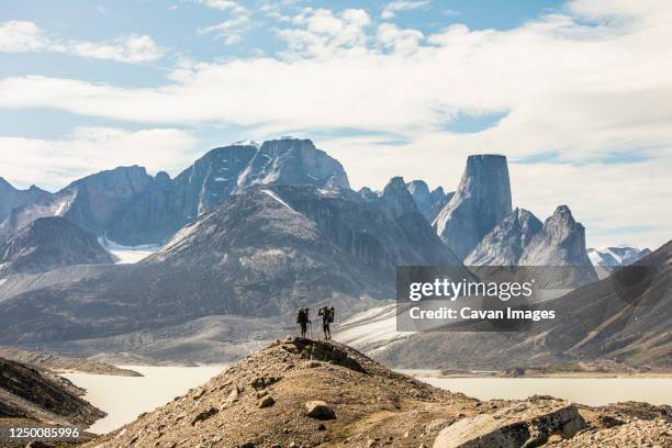 two backpackers stand on distant mountain ridge looking out at view. - nunavut foto e immagini stock