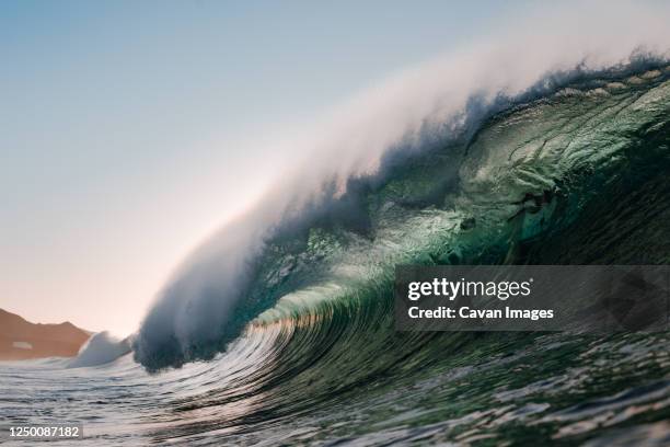 wave breaking under the sunset on the beach - tsunami fotografías e imágenes de stock
