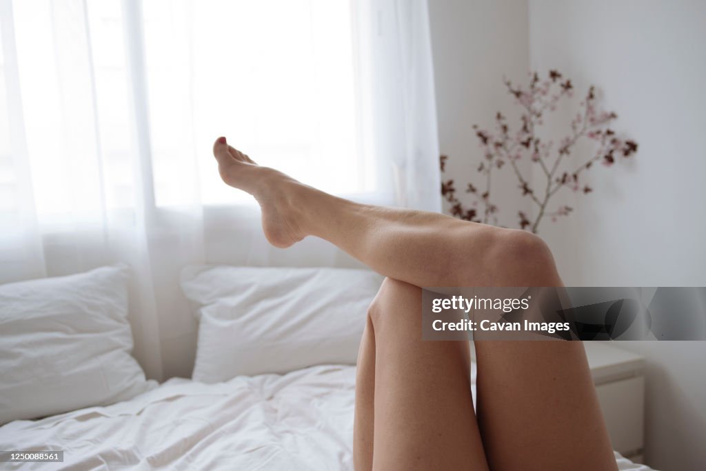 Close up of wome's legs lying on bed in white bedroom.