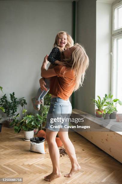 woman holds in hugs her laughing child in living room with lot plants - kids fashion stock pictures, royalty-free photos & images