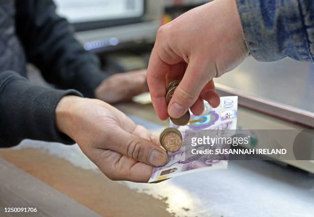 Customer uses a twenty pound sterling note and sterling coins to pay for goods inside a store in east London on March 31, 2023. - The UK economy...