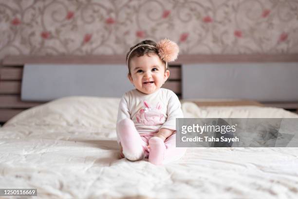a one year old baby girl sitting on a bed - baby girl stock pictures, royalty-free photos & images