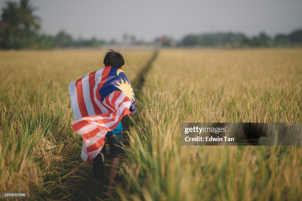Malaysia independence day an asian chinese young boy carrying malaysia flag at padi field enjoying morning sunlight and feel proud and happy running