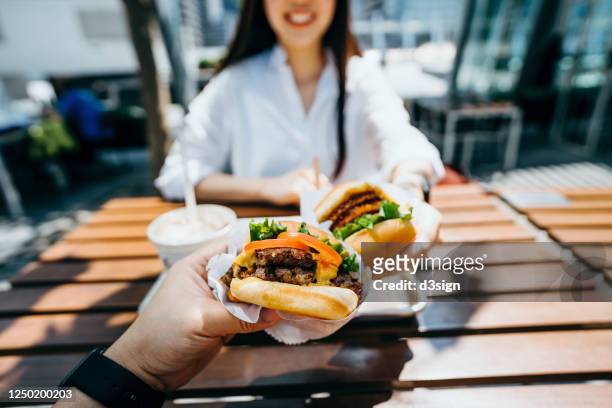 happy young asian couple eating beef burger with fries in an outdoor fast food restaurant - eating fast food stock-fotos und bilder