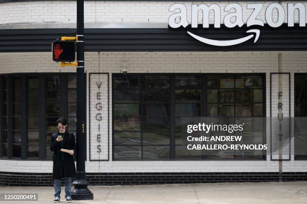 Man waits to cross the street near an Amazon Fresh store in Crystal City in Arlington, Virginia on March 31, 2023. - Amazon announced they are...