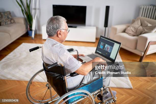 homme plus âgé s’asseyant dans le fauteuil roulant, utilisant l’ordinateur portatif - accessibilité aux personnes handicapées photos et images de collection