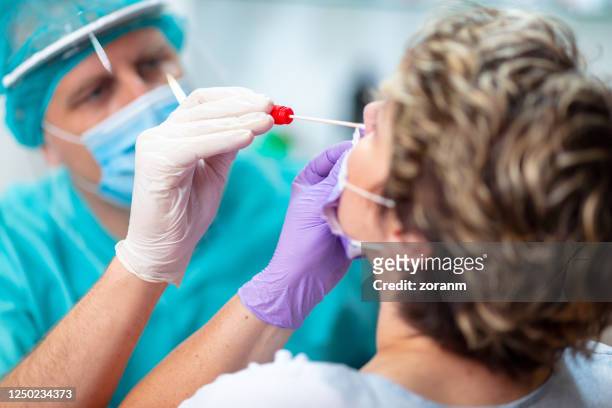 arzt trägt chirurgische handschuhe, die nasenabstrich von weiblicher patientin - coronavirus stock-fotos und bilder