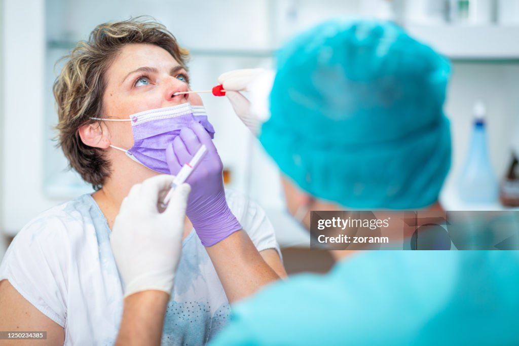 Médico tomando cotonete nasal de paciente do sexo feminino com máscara facial