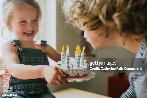 boy blowing out candles on a birthday cake as sister holds it out towards him - affectionate bildbanksfoton och bilder